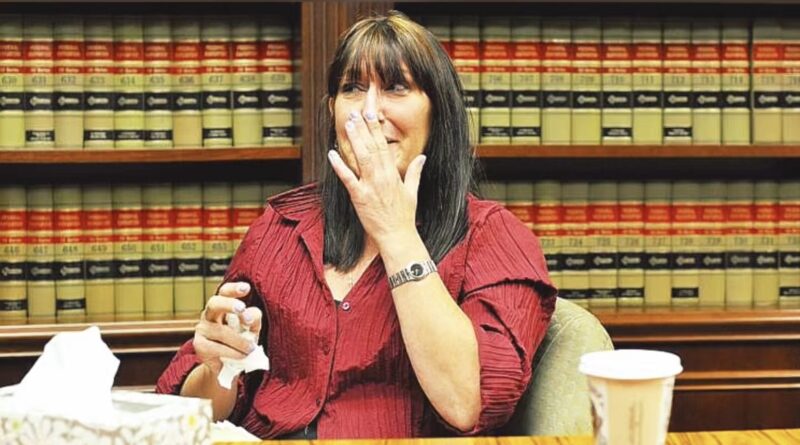 Debbie Stevens en larmes, tenant un mouchoir, lors d'une audition concernant son licenciement après son don de rein. Elle est assise devant une bibliothèque juridique.