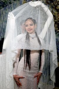 Lisa de Blackpink au Met Gala 2026. Elle porte une robe fourreau scintillante sous un voile de tulle cristallin. Deux bras de mannequin blancs et réalistes sont fixés à ses épaules et s'élèvent au-dessus de sa tête pour soulever le voile, créant une illusion de quatre bras.