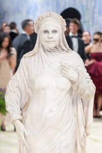 Heidi Klum au Met Gala 2026, entièrement transformée en une statue de marbre blanc de style antique. Son visage et son corps sont recouverts d'un maquillage et d'un tissu texturé qui imitent la pierre sculptée, incluant un voile drapé et une couronne de fleurs en marbre.