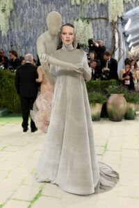 Jordan Roth au Met Gala 2026 portant une robe longue à col montant en velours gris perle. Une sculpture de mannequin grandeur nature, de la même couleur, est fixée à son dos et semble l'enlacer, ses bras passant par-dessus les épaules de Jordan pour rejoindre ses mains à l'avant.