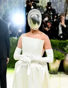 Katy Perry au Met Gala 2026. Elle porte une robe de bal blanche sans bretelles à la coupe architecturale épurée, accompagnée de longs gants blancs assortis. Son visage est entièrement dissimulé par un masque d'escrime futuriste doté d'une visière miroir bombée et d'un contour en maille blanche, reflétant les photographes environnants.